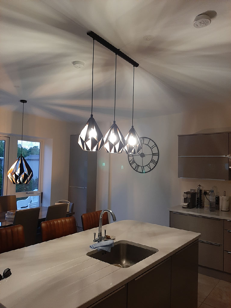 Three black and copper geometric pendants over a kitchen island in Mayo